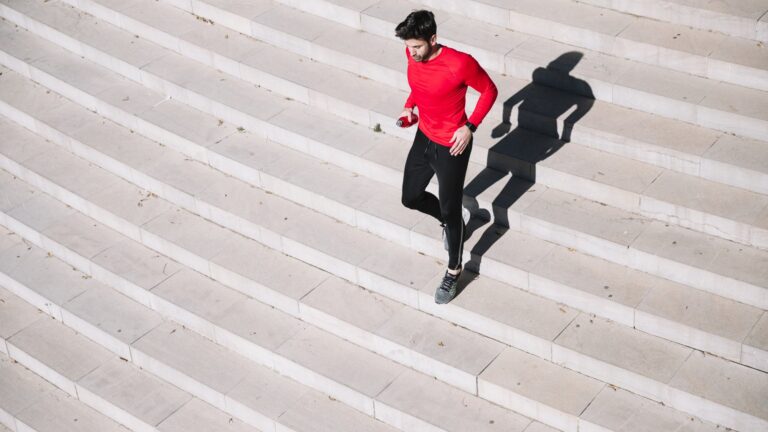 Mann in rotem Shirt joggt über eine helle Treppe, sein Schatten ist deutlich sichtbar.