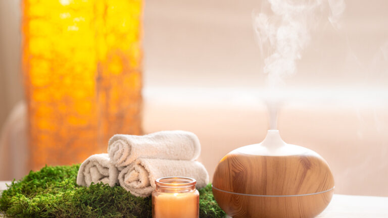 Ein Aromadiffusor aus Holz mit aufsteigendem Dampf, umgeben von Handtüchern, einer Kerze und grünem Moos.