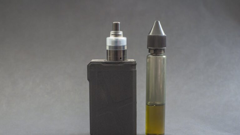 Ein Verdampfergerät links, daneben eine Flasche mit E-Liquid in einer transparenten Verpackung.