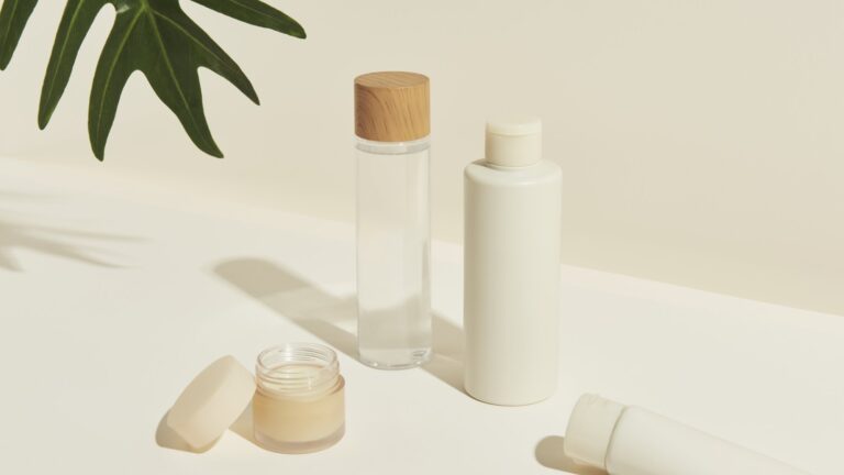 Verschiedene kosmetische Flaschen und Tiegel, darunter ein Glas mit Holzstoß, auf einem hellen Untergrund.