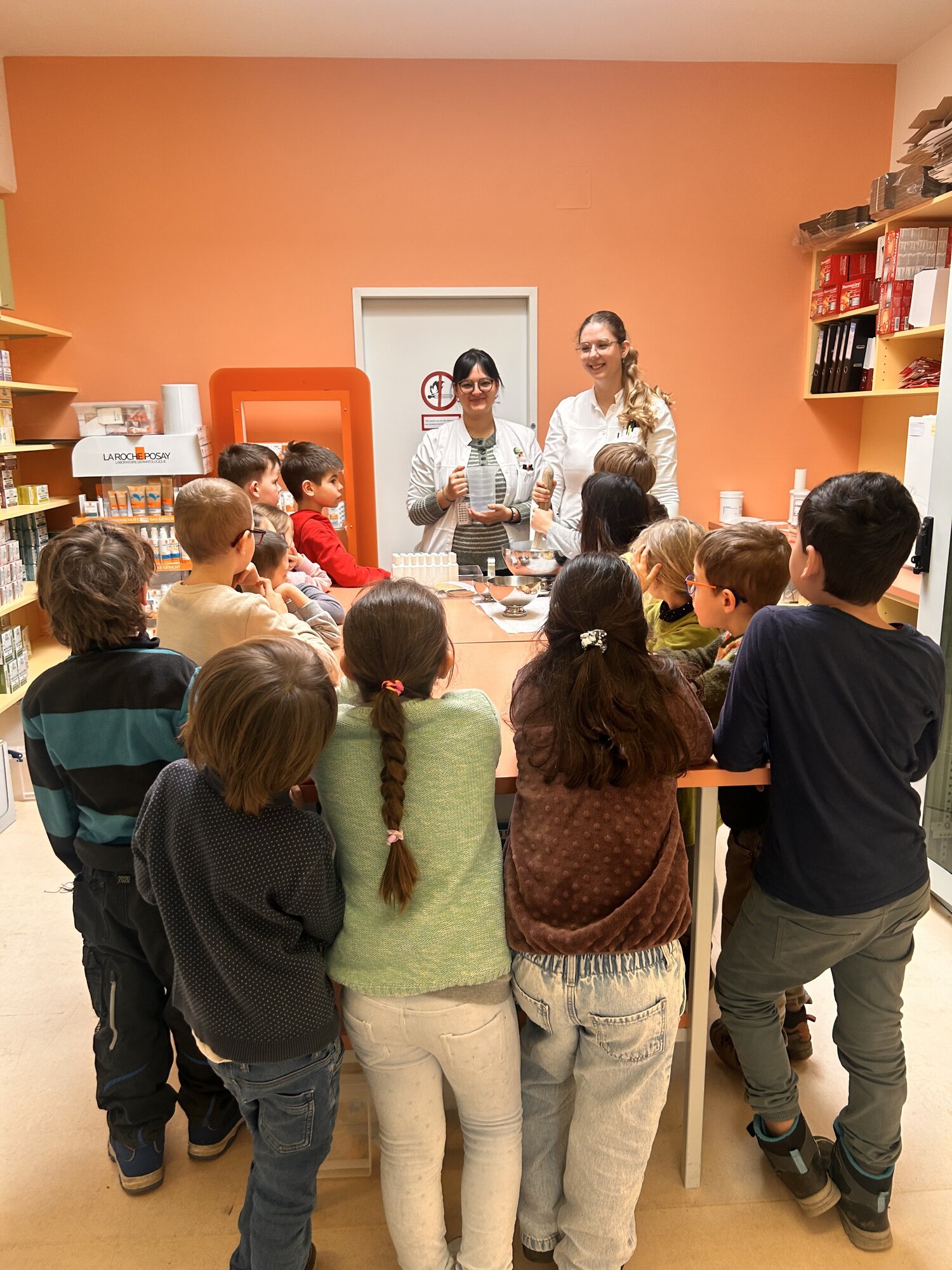 schulbesuch.jpg Zwei Erwachsene stellen einer Gruppe von Kindern an einem Tisch ein Experiment oder eine Aktivität vor in einem gemütlichen Raum.