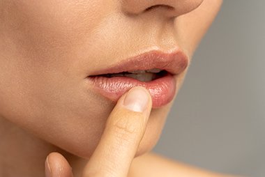Nahaufnahme eines Lippenbereichs, der von einem Finger berührt wird, mit glatter, rosiger Haut.