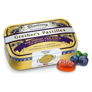 Blaubeerpastillen von Grether in einer goldenen Dose mit Aufschrift für Hals und Stimme, neben einer Blaubeere und einer Pastille.