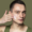 Ein Mann trägt Gesichtscreme auf seine linke Wange auf, Hintergrund ist ein einfarbiger, olivgrüner Farbton.