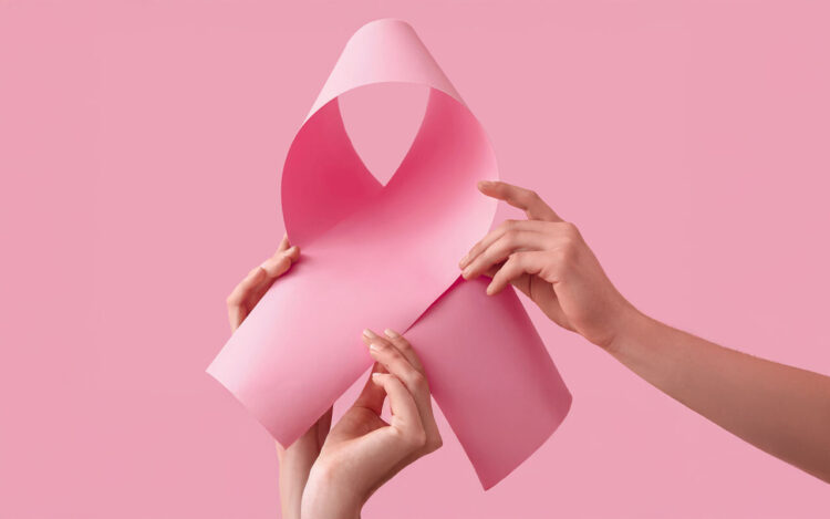 Zwei Hände halten ein rosa Papier, das zu einer Schleife geformt ist, vor einem pinken Hintergrund.