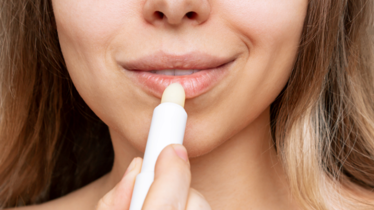 Frau trägt einen Lippenbalsam auf ihre Lippen auf, der in einem weißen Stick präsentiert wird.