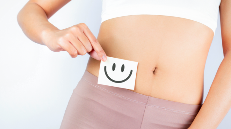 Eine Person hält eine Notiz mit einem lächelnden Gesicht vor den Bauch, auf weißem Hintergrund.