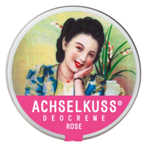 Runde Dose mit Deocreme "Achselkuss" in rosa, verziert mit einer lächelnden Frau und Pflanzenmotiv im Hintergrund.