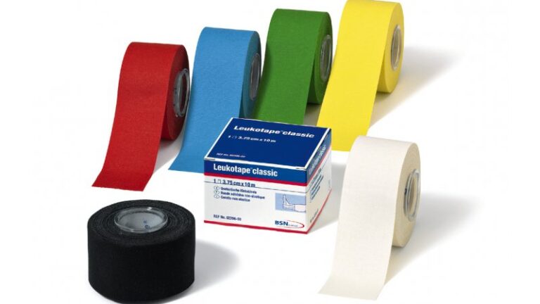 Verschiedene Rollen von Leukotape in den Farben Rot, Blau, Grün, Gelb und Weiß, daneben eine Verpackung mit Produktinformationen.