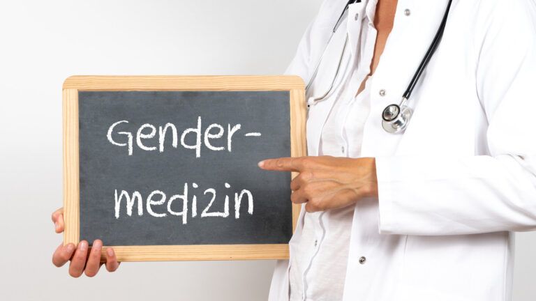 Eine Person in Arztkleidung hält eine Tafel mit der Aufschrift "Gendermedizin".